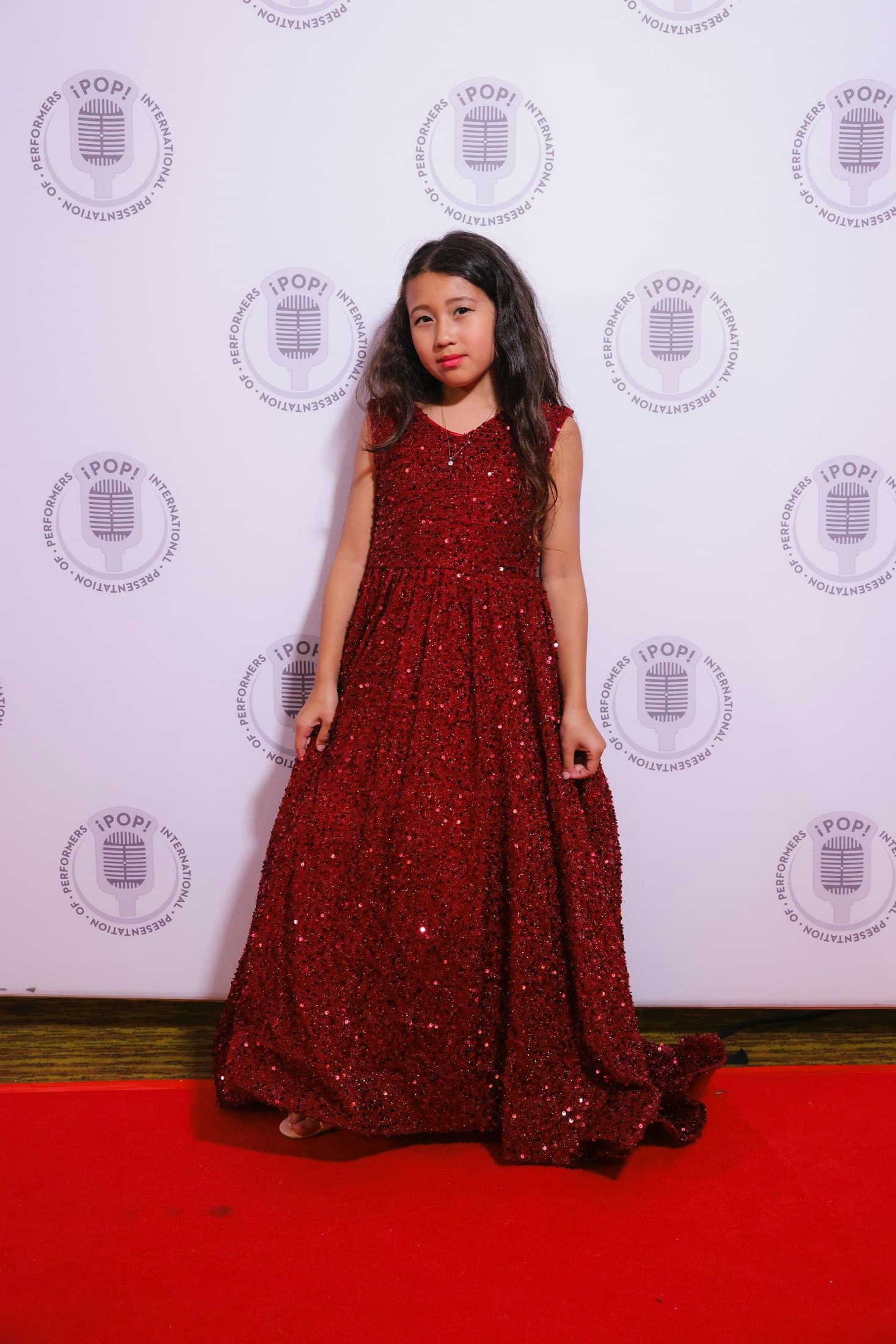 Kylie Akimoto in a red dress on a performance event backdrop